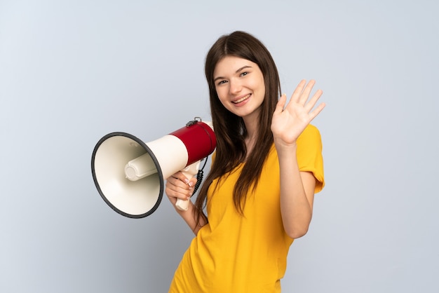 Jeune fille tenant un mégaphone et saluant avec la main avec une expression heureuse