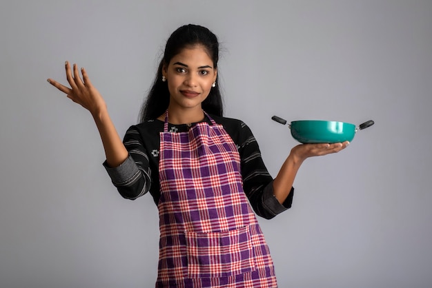 Jeune fille tenant et posant avec pan d'ustensiles de cuisine sur un mur gris