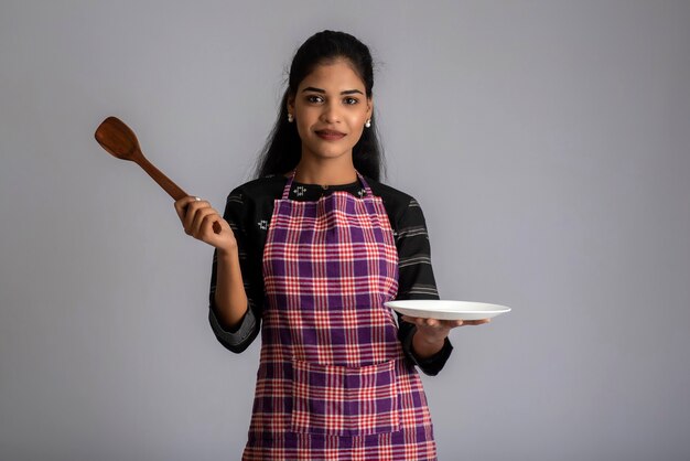 Jeune fille tenant et posant avec une spatule et une plaque d'ustensiles de cuisine sur un fond gris