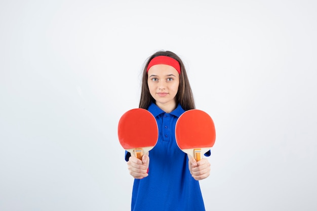 Une jeune fille tenant des raquettes de tennis de table sur un mur blanc