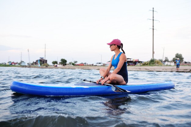 Jeune fille en tenue de sport assise sur un panneau de SUP