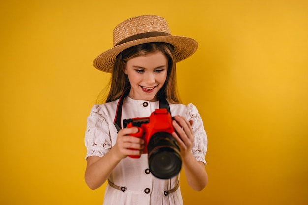 Une jeune fille tient un appareil photo rouge dans ses mains et regarde ses photos avec positif