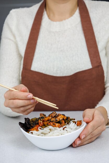 La jeune fille tient une assiette de nouilles de riz et de poulet dans ses mains Fond de cuisine maison sombre