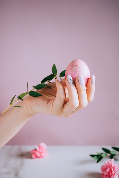 La jeune fille tient dans la main un oeuf de Pâques rose, fond rose et marbre, minimalisme, fleurs