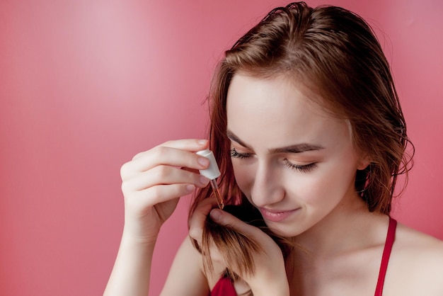 Jeune fille tient dans sa main le bout de ses cheveux et sa main droite les applique à l'huile jaune