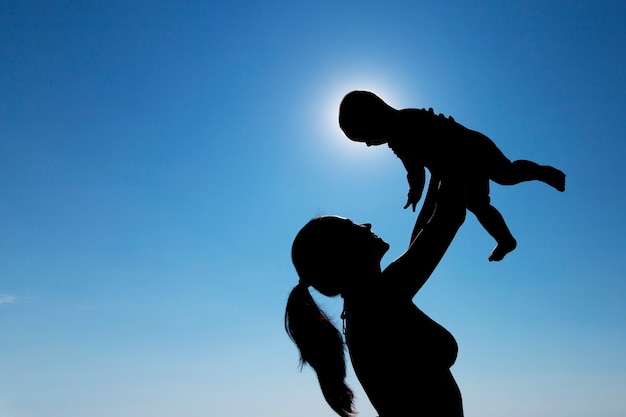 Une jeune fille tient un enfant dans ses bras contre le soleil. Photographie de silhouettes. photo de haute qualité