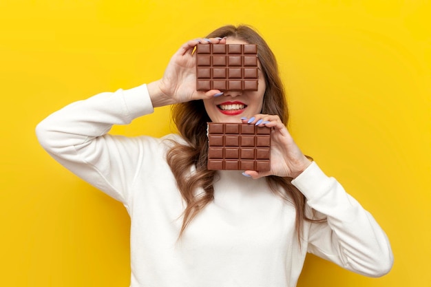 une jeune fille tient une grande barre de chocolat et couvre son visage sur un fond jaune isolé