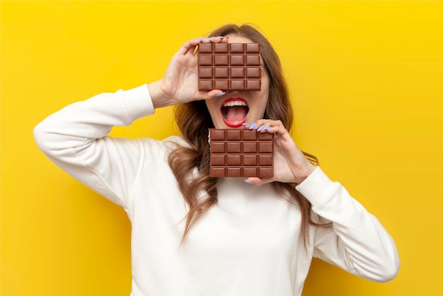 une jeune fille tient une grande barre de chocolat et couvre son visage sur un fond jaune isolé