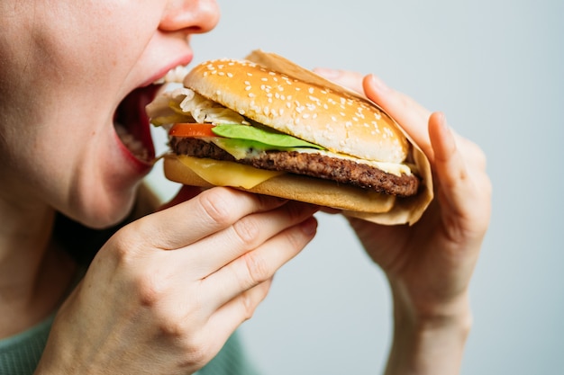 La jeune fille tient un hamburger avec ses mains et le mord.