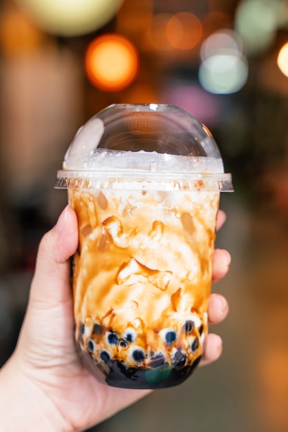 Jeune fille tient et montre une tasse de thé au lait à bulles de perles de tapioca aromatisé au sucre brun sur le marché de nuit de Taïwan en arrière-plan, gros plan, bokeh