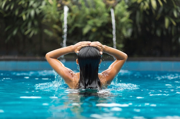 La jeune fille tient ses mains sur sa tête dans la piscine.