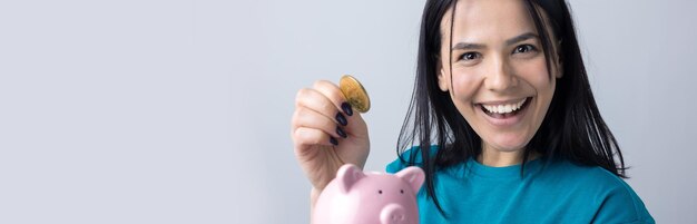 La jeune fille tient une tirelire rose et une pièce de monnaie dans ses mains Le concept de richesse et d'accumulation