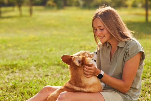 une jeune fille tient un Welsh Corgi joyeux et drôle dans ses bras dans un parc par temps ensoleillé le concept de chiens heureux