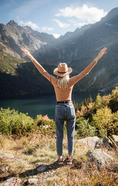 Jeune fille touristique dans un chapeau avec les mains levées au sommet des montagnes admire la nature
