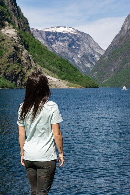 Jeune fille touristique méconnaissable sur le dos au pied du fjord, les bras levés, entourée de hautes montagnes à Gudvangen Norvège