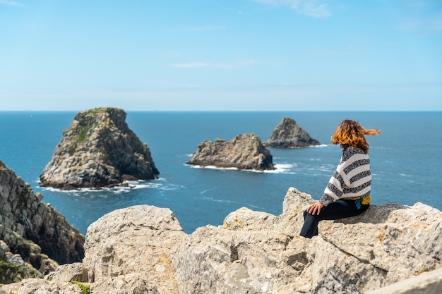 Une jeune fille touristique regardant la mer à Pen Hir Point sur la presqu'île de Crozon en Bretagne française, les trois célèbres îlots, France