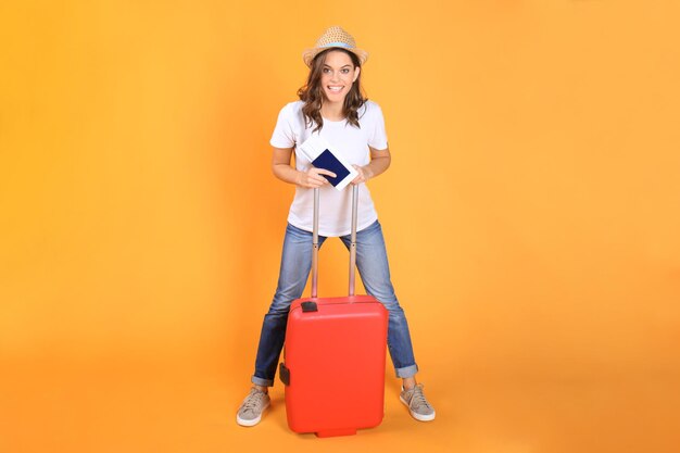 Jeune fille touristique en vêtements décontractés d'été, avec valise rouge, passeport, billets isolés sur fond beige