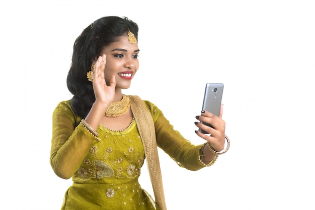 Jeune fille traditionnelle indienne à l'aide d'un téléphone mobile ou d'un smartphone isolé sur un mur blanc