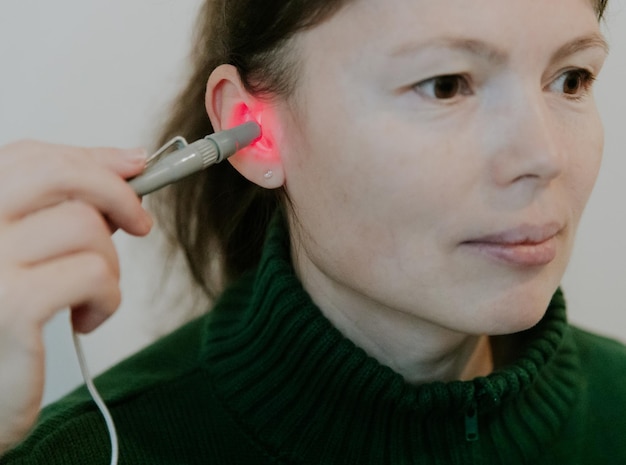 Une jeune fille traite son oreille avec un appareil à lumière infrarouge