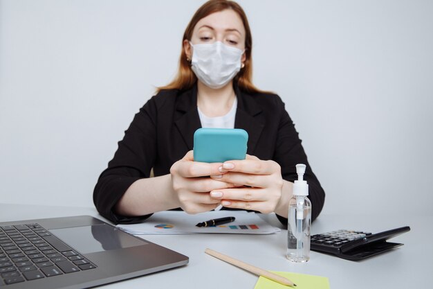 Jeune fille travaillant dans un masque facial sur le bureau. Travailler avec la calculatrice et noter quelque chose d'idée dans un smartphone