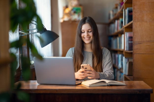 Jeune fille travaillant à la table dans une salle de classe universitaire Une étudiante lisant des livres prépare des recherches dans le cadre de son travail à domicile en utilisant des technologies modernes, un ordinateur portable et un téléphone portable avec Internet