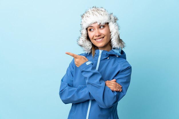 Jeune fille uruguayenne avec chapeau d'hiver sur le doigt de mur bleu sur le côté