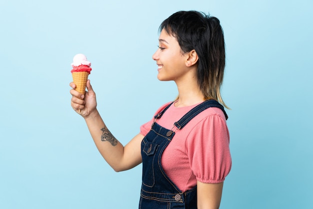 Jeune fille uruguayenne tenant une glace au cornet sur un mur bleu isolé avec une expression heureuse