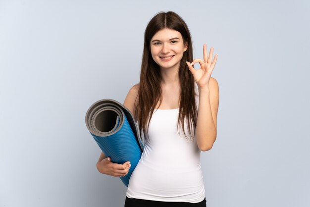 Jeune fille va à des cours de yoga tout en tenant un tapis montrant signe ok avec les doigts