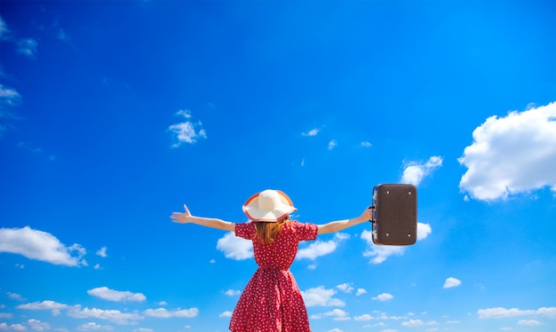 Photo jeune fille avec valise sur fond de ciel bleu