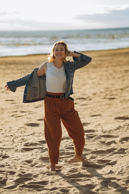 Jeune fille en veste en jean profiter du soleil sur la plage le soir d'été