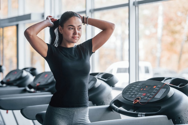 Jeune fille en vêtements de sport se préparant près du tapis roulant dans la salle de gym.