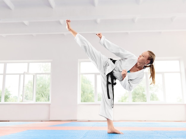 Jeune fille vêtue d'un kimono blanc effectuant un coup de pied élevé en arts martiaux.