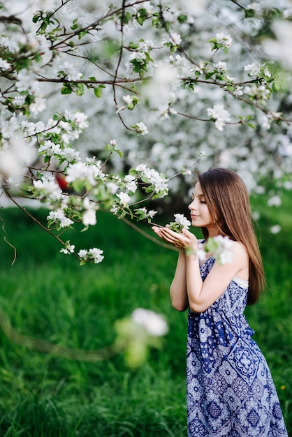 Une jeune fille vêtue d'une longue robe bleue apprécie l'arôme des pommiers en fleurs dans le jardin. Jardin fleuri. Saison des allergies.