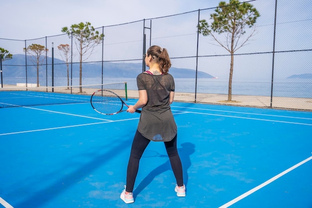 Jeune fille vêtue d'une robe bleu foncé joue au tennis sur le terrain avec un revêtement dur de bleu