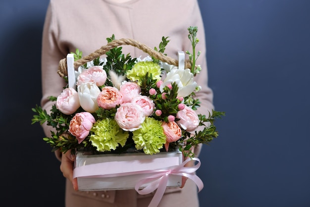 Une jeune fille vêtue d'une robe délicate tient une belle composition de fleurs dans une boîte, créée par un fleuriste. le concept d'une vente agréable pour des vacances.