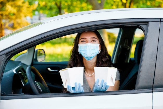 Jeune fille en voiture dans des gants médicaux et un masque détient le wok dans la boîte