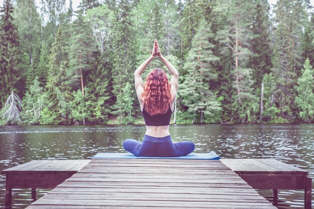 Jeune fille yogi pratiquant le yoga assise dans une variation de la posture du visage de vache Gomukhasana sur la jetée d'un magnifique lac Concept de vie saine et d'équilibre naturel