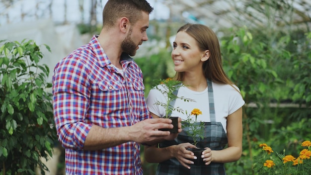 Jeune fleuriste sympathique parlant au client et lui donnant des conseils tout en travaillant dans le jardin