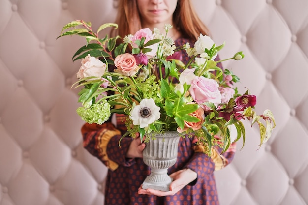 Photo jeune fleuriste tenant un bouquet d'oeillets pastels et d'eucalyptus contre un mur rose.