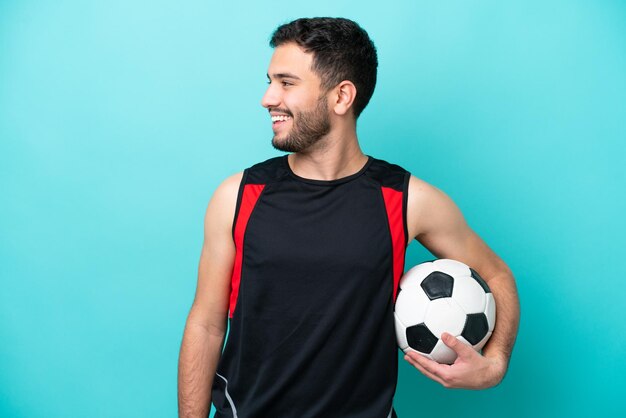 Jeune footballeur homme brésilien isolé sur fond bleu regardant à côté