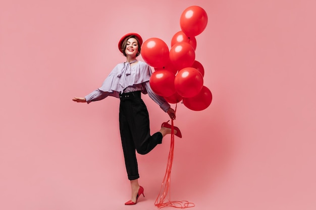 Jeune française en béret rouge et chemisier bleu sautant sur fond rose avec des ballons rouges
