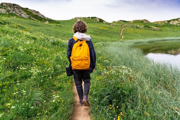 Jeune garçon adolescent avec sac à dos jaune marchant dans les hautes montagnes des Alpes françaises. Notion de randonnée. Activités estivales.