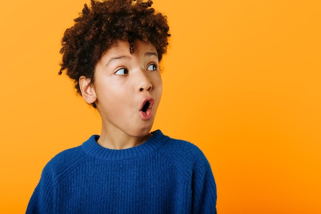 Un jeune garçon afro-américain étonné exprime sa surprise avec la bouche ouverte sur un fond orange vif.