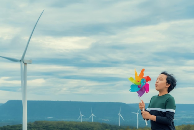 Jeune garçon asiatique progressiste jouant avec un jouet moulin à vent à la ferme éolienne