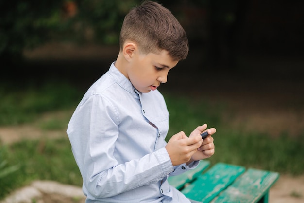 Jeune garçon assis sur le banc et jouer à des jeux en ligne pendant les vacances scolaires