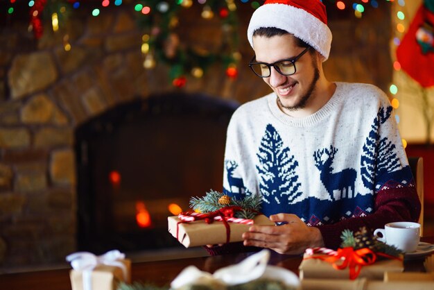 Jeune garçon attachant le ruban sur le cadeau de Noël L'humeur du Nouvel An lumières floues feu de foyer en arrière-plan