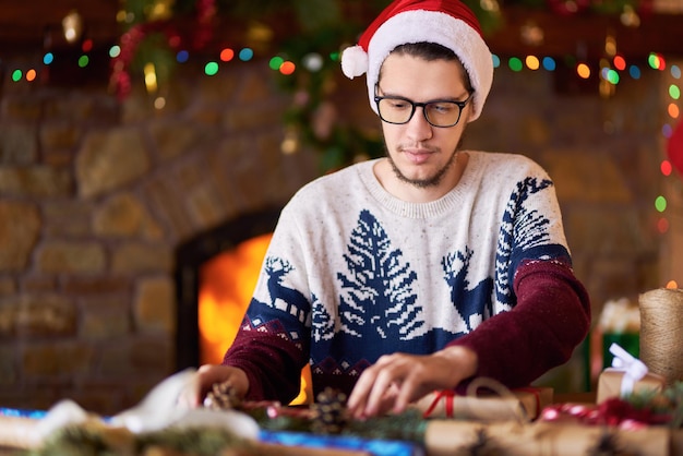 Jeune garçon attachant le ruban sur le cadeau de Noël L'humeur du Nouvel An lumières floues feu de foyer en arrière-plan