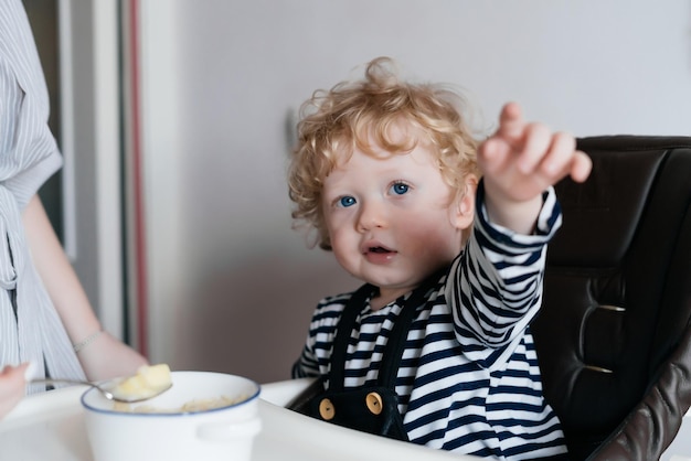 Jeune garçon aux yeux bleus curieux assis dans la cuisine en train de manger un désordre utile avec sa mère