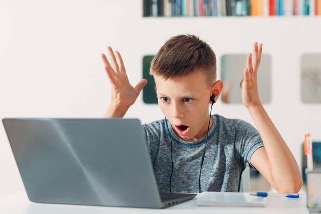 Jeune garçon en casque assis à table avec ordinateur portable et se préparer à l'école