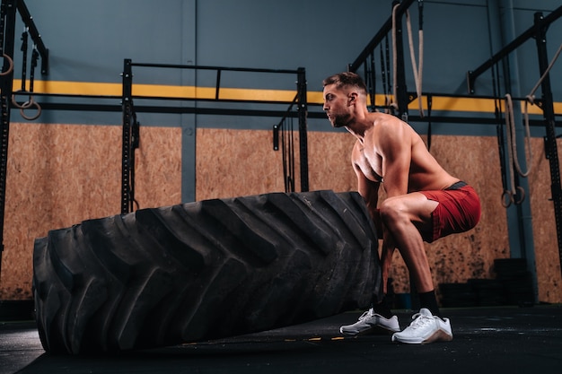 Jeune garçon caucasien dans ses 30s fitness soulevant une roue pour faire des exercices